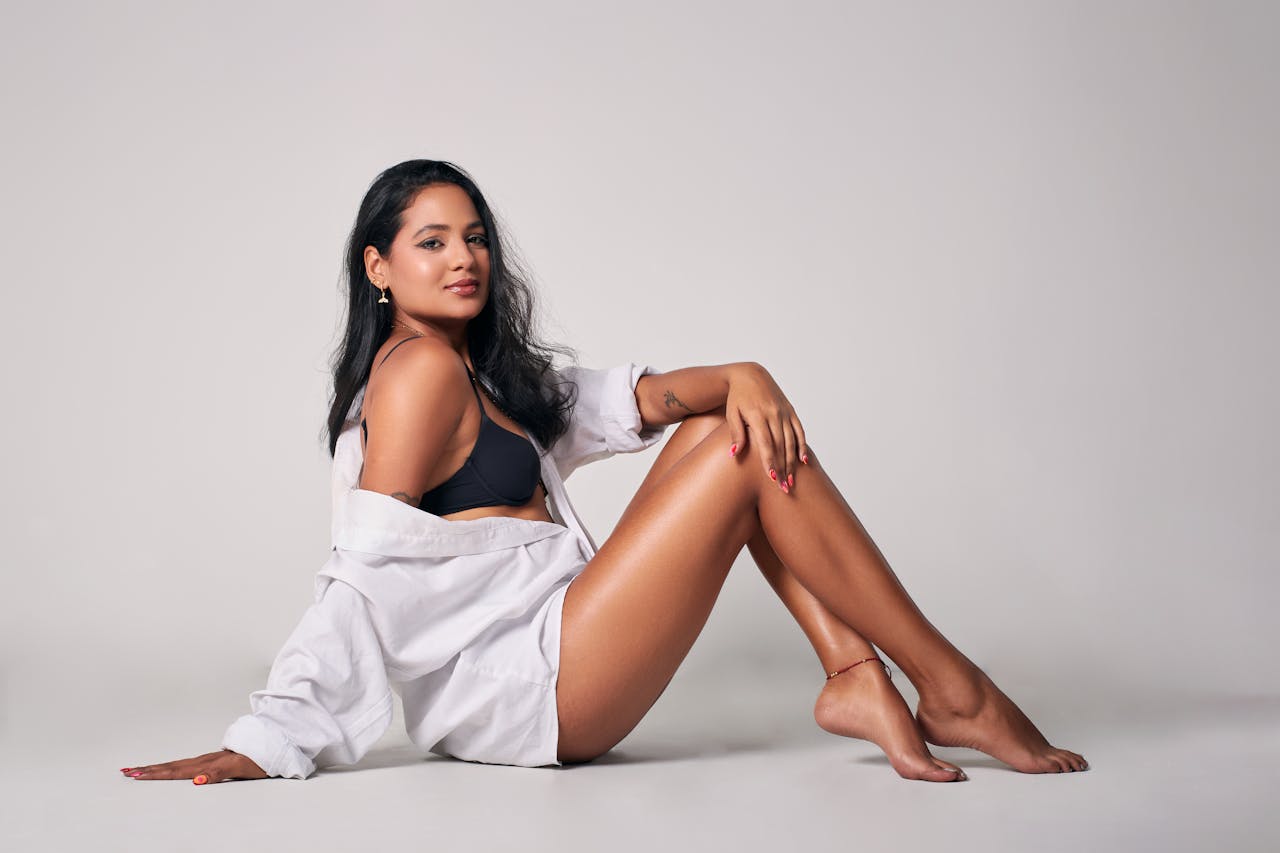 Confident woman in black bikini and white shirt posing elegantly in studio setting.